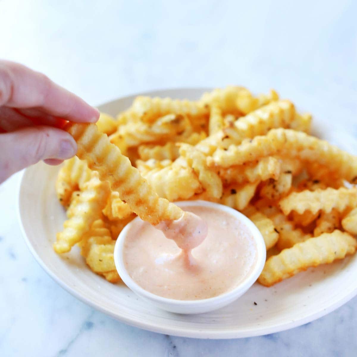 A bowl of creamy, orange-hued Raising Cane's copycat sauce with a side of golden french fries.