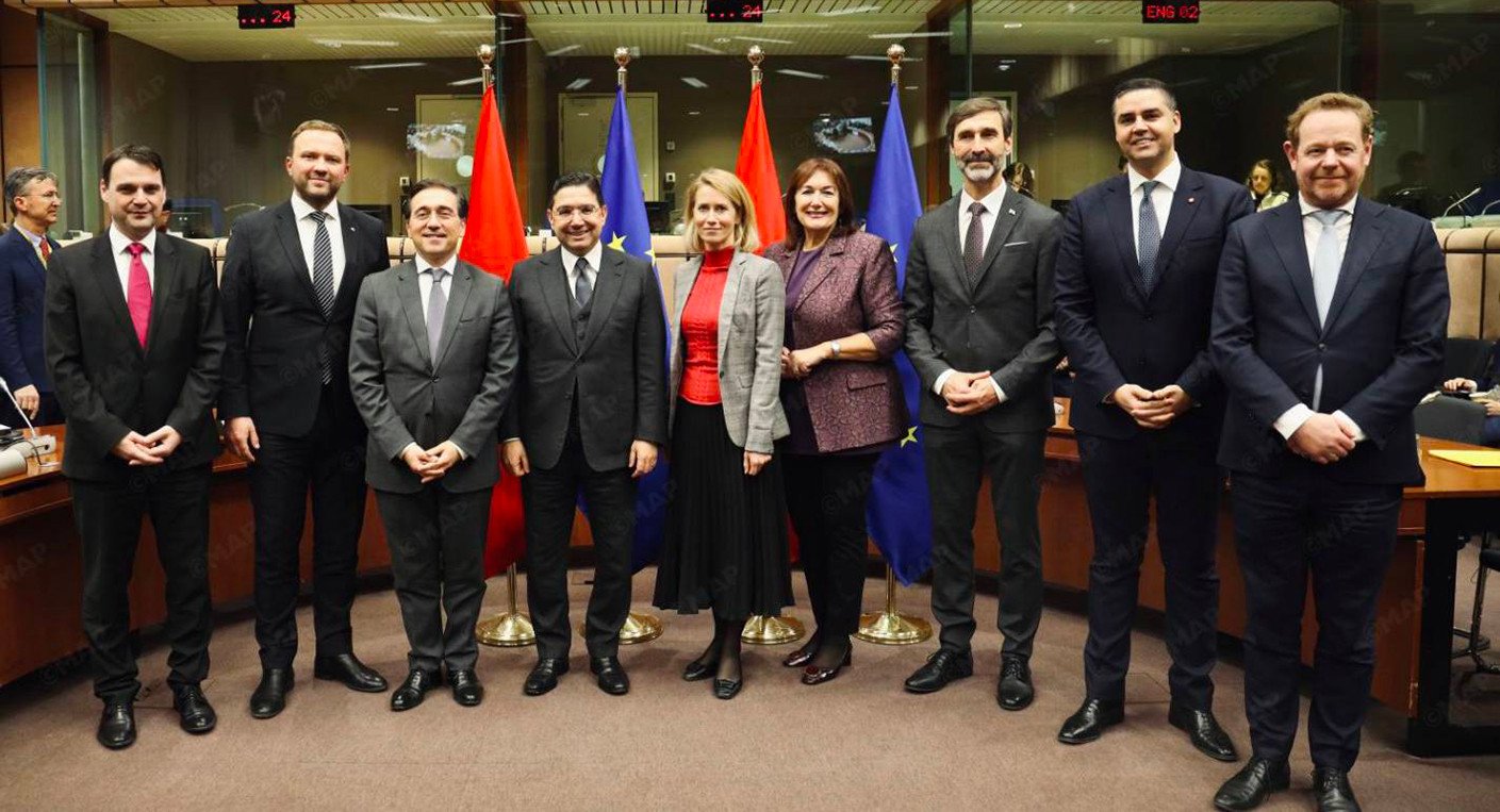 Vue aérienne du Sahara avec un drapeau marocain symbolisant l'autonomie sous souveraineté marocaine, entouré de drapeaux de l'Union Européenne.