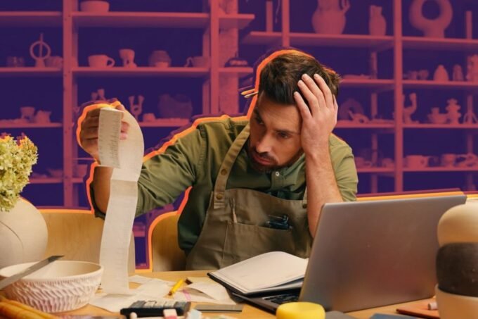 A small business owner looking at financial documents with a calculator and laptop, symbolizing tax planning and financial management.