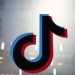 A smartphone displaying the TikTok logo, with a blurred background of children or young people, symbolizing the debate around age verification on social media platforms.