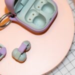 A pair of Sony LinkBuds Clip earbuds in green, shown clipped onto an ear, with their customizable charging case in the background.