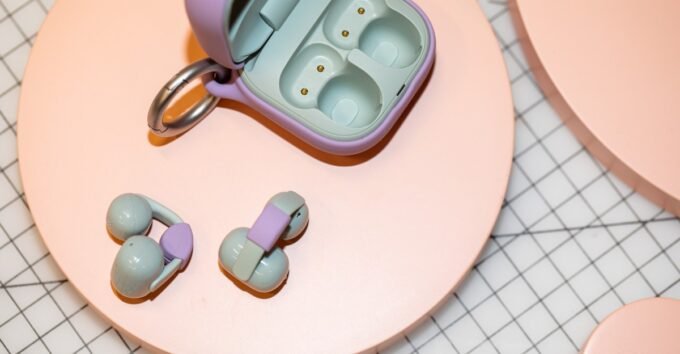 A pair of Sony LinkBuds Clip earbuds in green, shown clipped onto an ear, with their customizable charging case in the background.