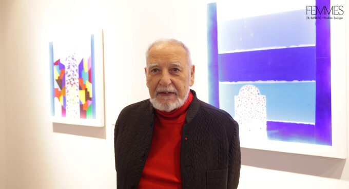 Tahar Ben Jelloun devant un de ses vitraux colorés, l'œuvre baignée de lumière.