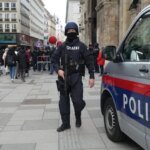 Un logo stylisé symbolisant la coopération internationale en matière de sécurité, avec les drapeaux de l'Autriche et du Maroc entrelacés, sur fond de carte du monde légèrement floue. Le tout est entouré d'un halo lumineux, évoquant la vigilance et le succès des opérations antiterroristes.