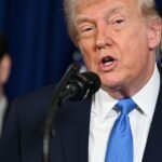 Donald Trump speaking at a press conference with a backdrop of the American flag, discussing Venezuela's oil economy.