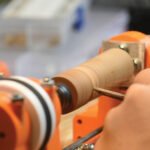 A close-up view of a partially assembled 3D-printed wood lathe, showing its wooden base and red 3D-printed components.
