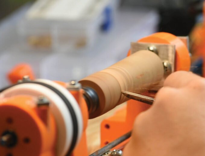 A close-up view of a partially assembled 3D-printed wood lathe, showing its wooden base and red 3D-printed components.