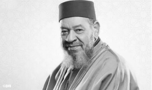 Portrait en noir et blanc d'Abdelhadi Belkhayat, le grand artiste marocain, souriant et élégant, micro à la main.