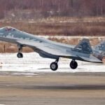 Un avion de chasse furtif Sukhoi Su-57 avec un camouflage 'Belaya Akula' (requin blanc) survolant un paysage désertique, symbolisant la présence potentielle en Algérie et les implications géopolitiques.