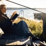 A person writing in a leather-bound journal with a vintage camera and a cup of coffee nearby, symbolizing a return to analog hobbies.