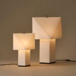 Aplat Table Lamp by CPRV for HAY, a folded paper lamp with a minimalist design, sitting on a table.