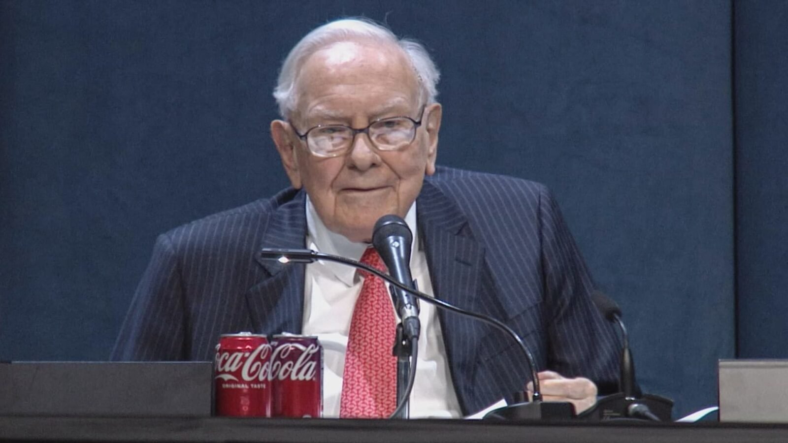 Warren Buffett reviewing Berkshire Hathaway's investment portfolio, with American Express and Apple stock charts in the background