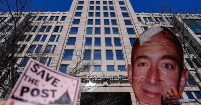 Demonstrators hold a "Save The Post" sign next to a cutout image of Jeff Bezos during a rally outside The Washington Post headquarters in Washington, DC.