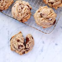 Freshly baked brown butter chocolate chip cookies, golden brown with melted chocolate chips and a sprinkle of flaky sea salt, cooling on a wire rack.
