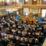 A 3D printer in the process of manufacturing a firearm component, with a blurred background of legislative documents.