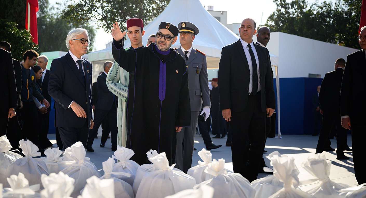 Sa Majesté le Roi Mohammed VI, accompagné de SAR le Prince Héritier Moulay El Hassan, lance l'opération nationale Ramadan 1447 à Salé, remettant symboliquement des paniers alimentaires à des familles bénéficiaires, entouré de bénévoles.