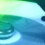 Close-up of a curling stone gliding on ice with a broom sweeping ahead, showcasing advanced sports technology.