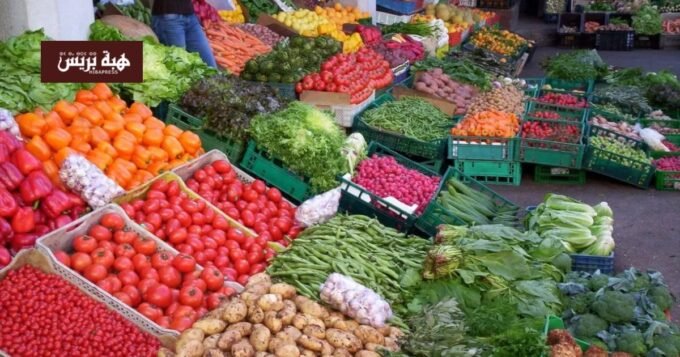 صورة تعرض مجموعة متنوعة من الخضر والفواكه الطازجة في سوق مغربي، مع التركيز على وفرة المنتجات وانخفاض أسعارها.