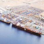 صورة جوية لميناء العقبة الأردني تظهر حركة السفن والحاويات، مع خلفية للمدينة.