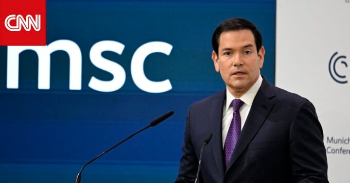 ماركو روبيو يلقي كلمة في مؤتمر ميونيخ للأمن، مع خلفية أعلام أمريكية وأوروبية ترمز للتحالف عبر الأطلسي.