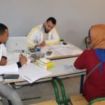 صورة تظهر فريقاً طبياً يقدم خدمات صحية للمواطنين في قافلة طبية بجماعة تلوات، ورزازات، مع خلفية جبلية.