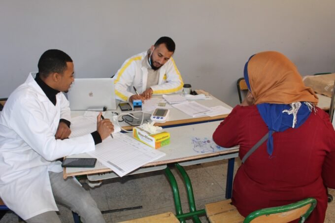 صورة تظهر فريقاً طبياً يقدم خدمات صحية للمواطنين في قافلة طبية بجماعة تلوات، ورزازات، مع خلفية جبلية.