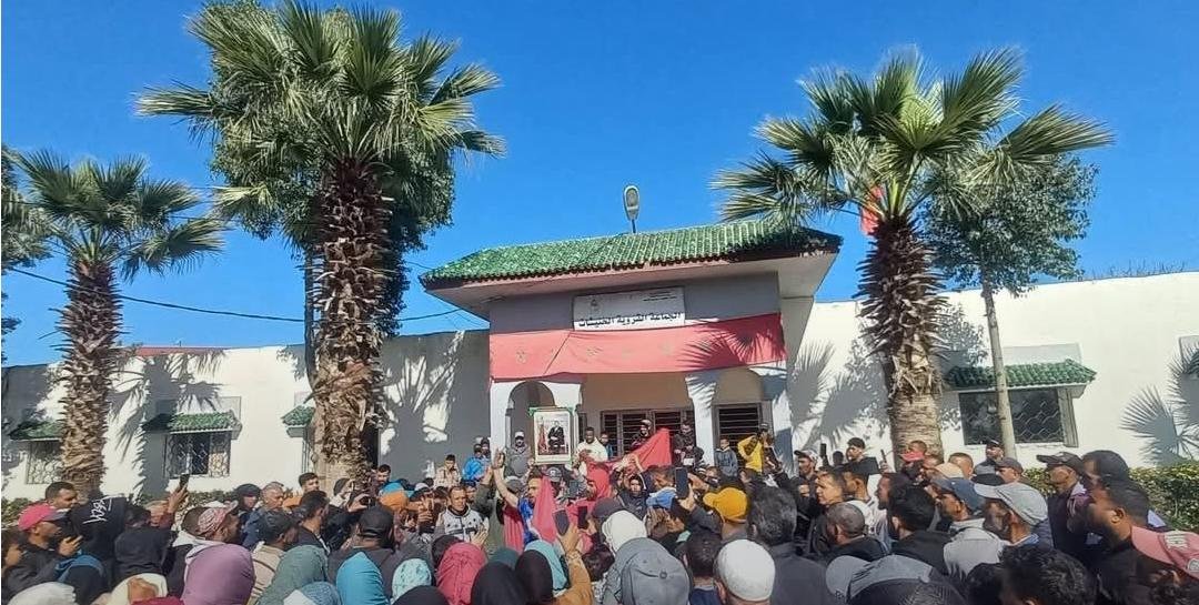 صورة لمسيرة احتجاجية لسكان دواوير الخنيشات المتضررين من الفيضانات في سيدي قاسم، تظهر مشاركة رجال ونساء وأطفال.