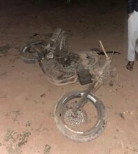 صورة لدراجة نارية متضررة في موقع حادث سير بمدار دائري في أولاد تايمة، مع وجود سيارات الإسعاف والشرطة.