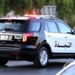 صورة لحقيبة ملقاة على جانب الطريق في منطقة حضرية، مع وجود عناصر أمنية في الخلفية