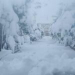 مشهد لمدينة نيويورك مغطاة بالثلوج الكثيفة خلال عاصفة شتوية، مع سيارات تسير ببطء في الشوارع.