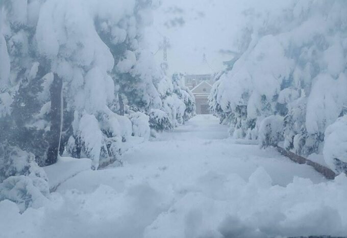 مشهد لمدينة نيويورك مغطاة بالثلوج الكثيفة خلال عاصفة شتوية، مع سيارات تسير ببطء في الشوارع.