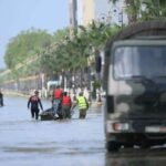 Vue aérienne d'une zone inondée au Maroc, avec des maisons partiellement submergées et des champs sous l'eau, symbolisant les crues et l'attente de la décrue.