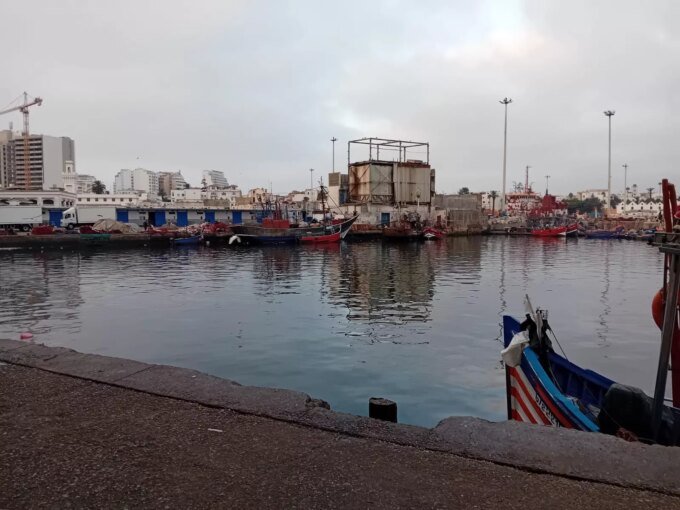 Vue aérienne du port de pêche de Casablanca, montrant des bateaux amarrés et les infrastructures portuaires sous un ciel clair.
