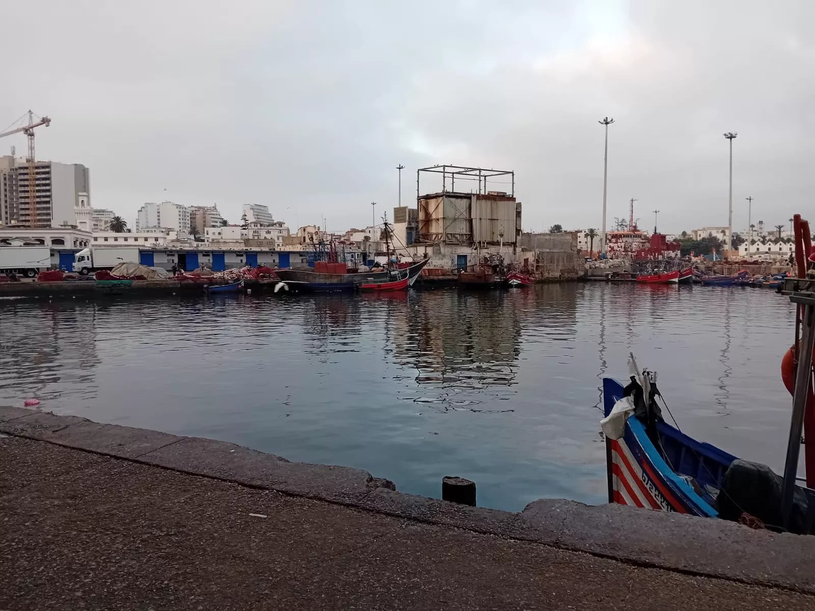 Vue aérienne du port de pêche de Casablanca, montrant des bateaux amarrés et les infrastructures portuaires sous un ciel clair.