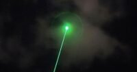 An anti-drone laser system aiming at a drone in the sky over a city skyline.