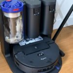 Dyson Spot+Scrub Ai, robot aspirateur laveur haut de gamme, posé sur un sol propre, mettant en avant son design futuriste et ses brosses de nettoyage.
