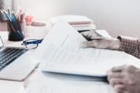 A person reviewing a thick franchise agreement document with a magnifying glass, symbolizing strategic analysis.