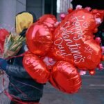 A group of diverse women laughing and toasting with cocktails at a festive Galentine's Day celebration, surrounded by balloons and decorations.