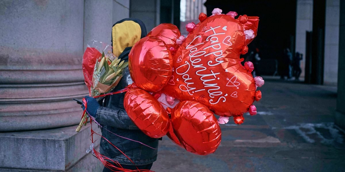 A group of diverse women laughing and toasting with cocktails at a festive Galentine's Day celebration, surrounded by balloons and decorations.