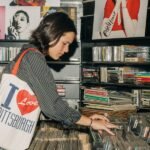 A young person holding a vinyl record, surrounded by books and a record player.