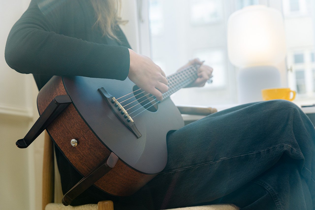 The Openhagen Harmoni Guitar with its magnetic stand and Nordic horse capo, showcasing its elegant mahogany finish.