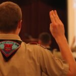 Defense Secretary Hegseth speaking at a podium, with a blurred background suggesting a military or official setting.