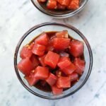 The Ultimate Homemade Poke Sauce: Your Key to Authentic Hawaiian Bowls 2 Freshly made poke sauce in a glass bowl, surrounded by its key ingredients: soy sauce, rice vinegar, sesame oil, sriracha, fresh ginger, garlic cloves, and lime halves.