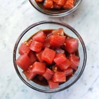 Freshly made poke sauce in a glass bowl, surrounded by its key ingredients: soy sauce, rice vinegar, sesame oil, sriracha, fresh ginger, garlic cloves, and lime halves.