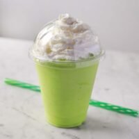 A vibrant green homemade Shamrock Shake topped generously with whipped cream and a cherry, served in a clear glass.