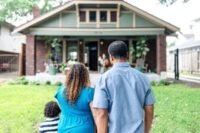 A diverse group of people looking at a new house, symbolizing hope for affordable homeownership.