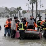 Vue aérienne d'une zone inondée au Maroc, avec des habitations entourées d'eau et des équipes de secours en action.
