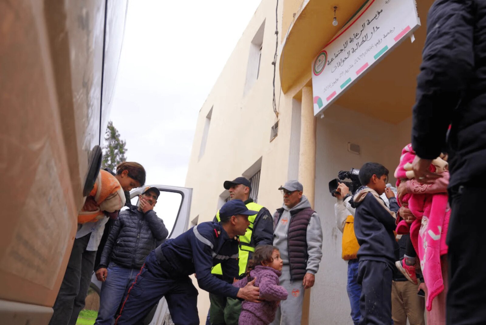 Une femme souriante, Fatima Zahra, devant un paysage urbain, symbolisant l'action humanitaire et la solidarité.