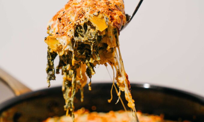 A warm, golden-brown kale artichoke dip topped with melted cheese and everything bagel seasoning, served in a pan.