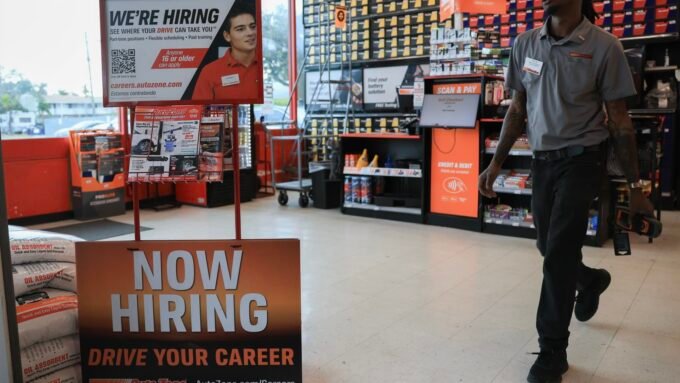 A 'Now Hiring' sign displayed at an AutoZone store, symbolizing current labor market conditions.